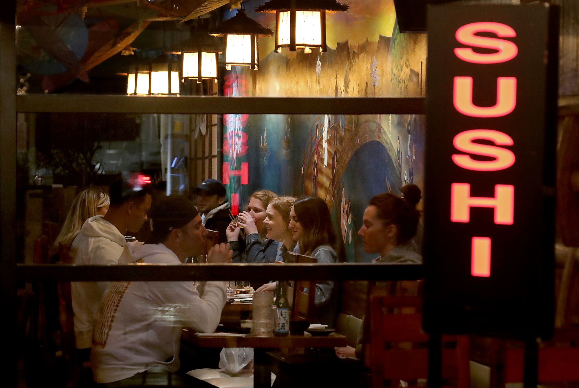 People are seated facing one another near a sign that reads Sushi 