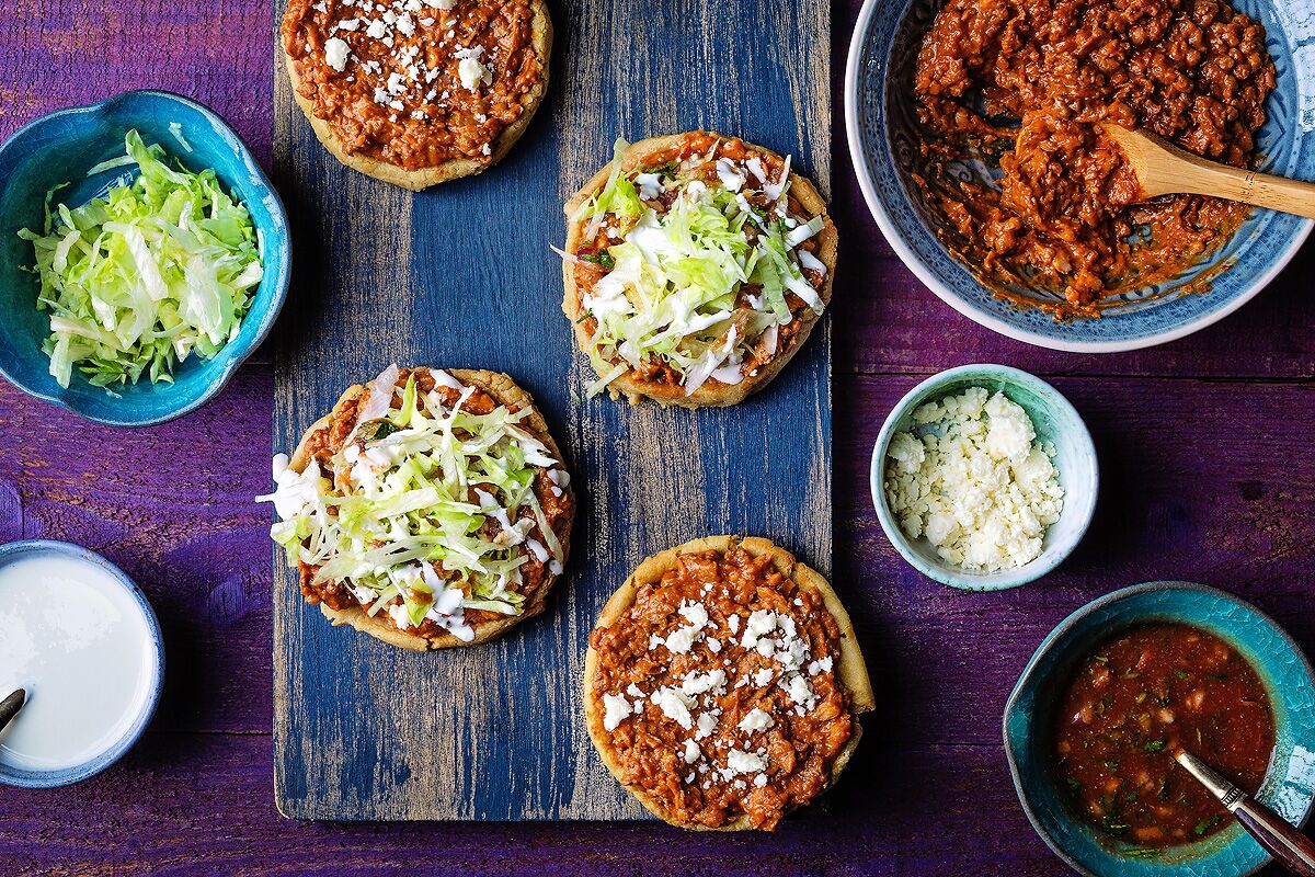 Mexican sopes on a board surrounded by bowls of garnishes.
