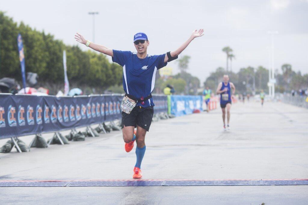Peter Yeh celebrates as he crosses the finish line of the half-marathon at the 13th annual US Bank OC Marathon at the OC Fairgrounds in Costa Mesa on Sunday.