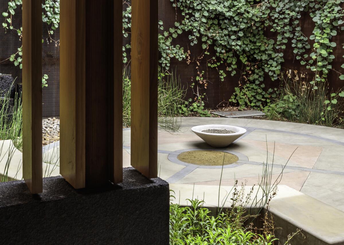 A view through a threshold shows a small garden, draped in plants, with a concrete ceremonial urn at center.