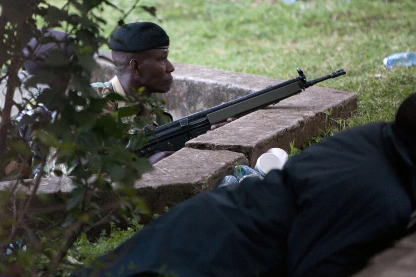 Kenyan security personnel take cover outside the Westgate mall in Nairobi, the capital, after firing started inside the mall early Monday.