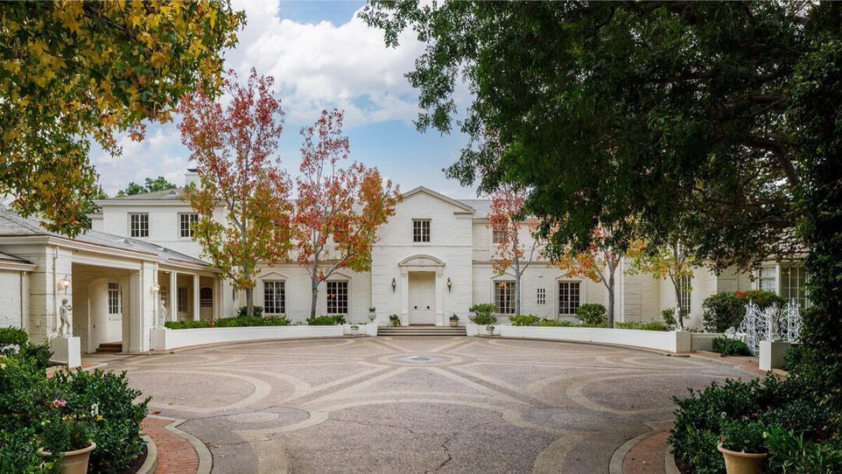 An expansive motor courtyard in front of a white, classical two-story mansion.