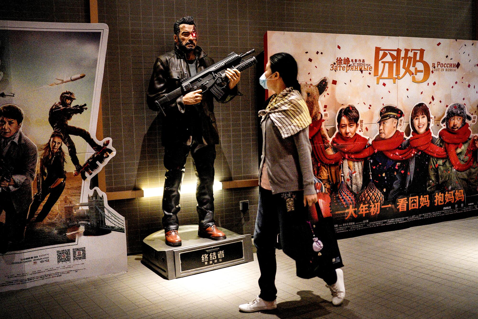 A woman in a mask walks by movie posters and a full-size figure of a film character holding a weapon.