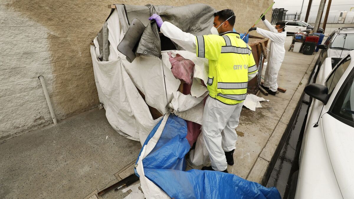 Jesus Sanchez, left, and Javier Villarreal of the L.A. Sanitation Bureau clean up a homeless encampment at 41st Place and Alameda Street on May 23.