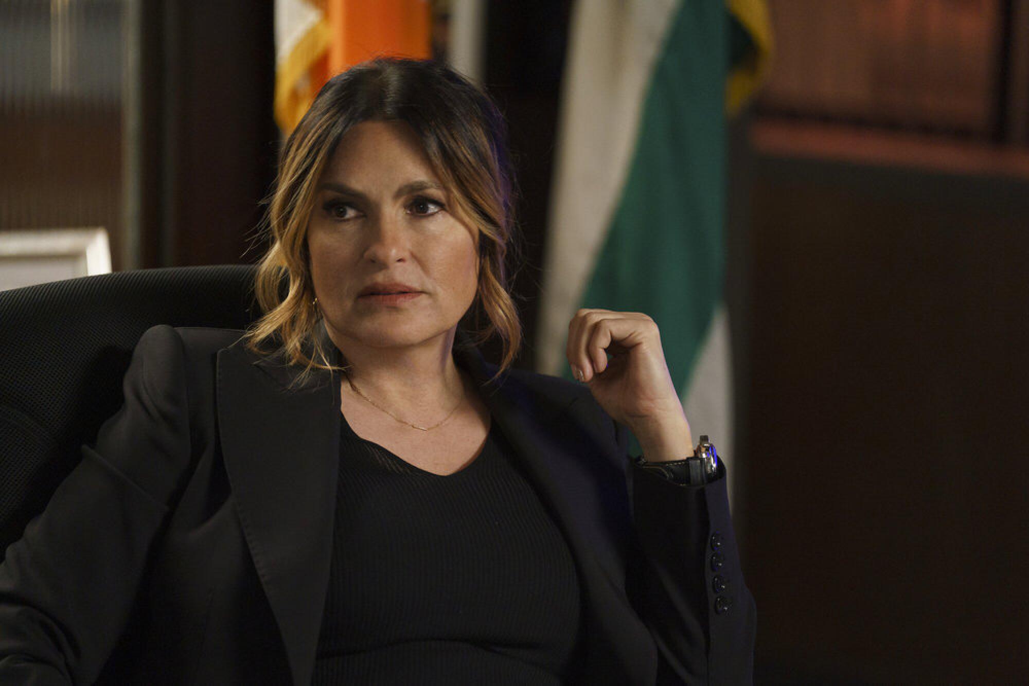 Olivia Benson, who is wearing a black shirt and blazer, sits in a dark chair.