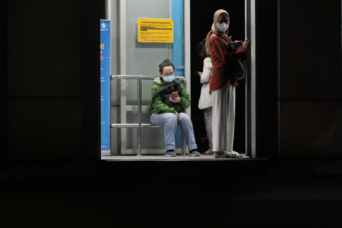 People wearing masks to curb the spread of the coronavirus wait at a bus stop in Jakarta, Indonesia, Tuesday, May 17, 2022. Indonesia will lift its outdoor mask mandate because its COVID-19 outbreak appears to be waning, President Joko Widodo said Tuesday. (AP Photo/Dita Alangkara)