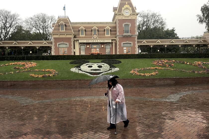ANAHEIM, CALIF. -- THURSDAY, MARCH 12, 2020: A Disneyland employee walks through the entrance to Disneyland amid rain showers in Anaheim, Calif., on March 12, 2020. Disneyland will temporary close the Disneyland Resort in Anaheim in response to the expanding threat posed by the Coronavirus Pandemic. The closure takes effect Saturday and lasts through the end of March. Disneyland and Disney California Adventure will close Saturday morning through the end of the month in response to Gov. Gavin Newsom and state health officials' recommendation that gatherings of 250 or more people be canceled across the state, company officials said. (Allen J. Schaben / Los Angeles Times)