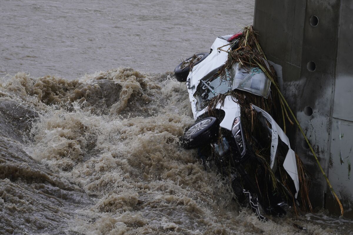 A smashed car wedged against a concrete pillar in raging river waters