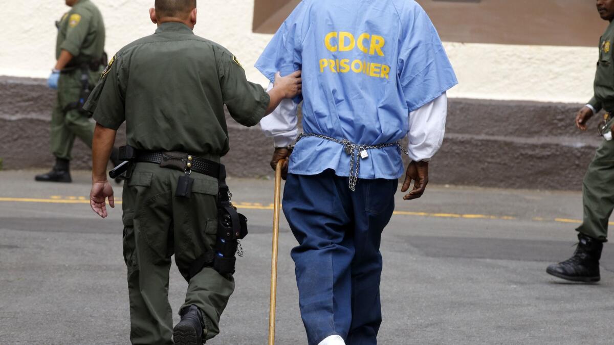 A death row inmate with a cane is escorted across the yard on his way to a morning appointment at San Quentin State Prison.