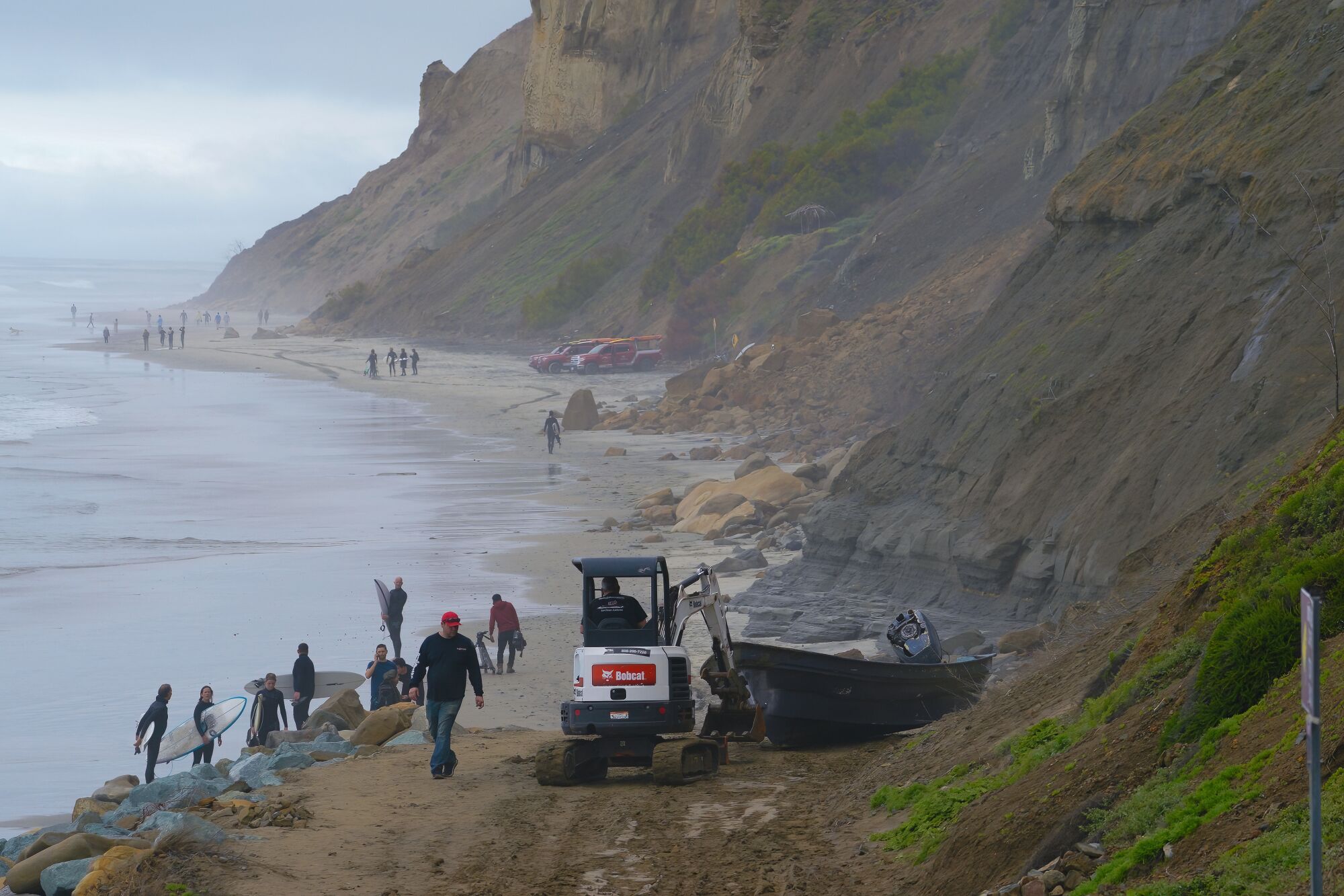 Surfers walk past a salvage crew beginning to haul a smuggling panga on Sunday, March 12, at Black's Beach. 
