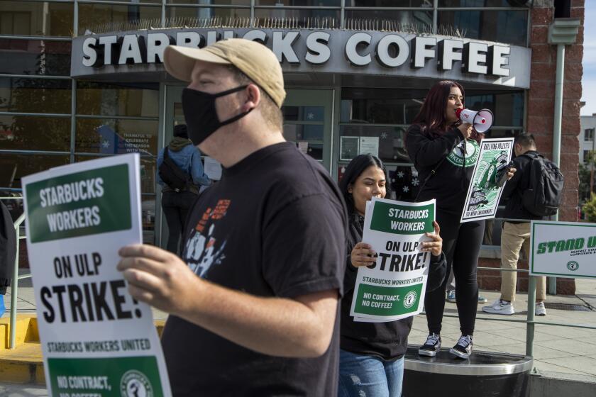 LOS ANGELES, CA - December 16, 2022: Employees, supporters and labor organizers hold signs as they strike a Starbucks location on S. Central Ave. downtown, one of about 100 Starbucks stores across America on strike for the next three days, as the union attempts to turn up the pressure in it year-long battle with the coffee retailer on Friday, Dec. 16, 2022 in Los Angeles, CA. (Brian van der Brug / Los Angeles Times)