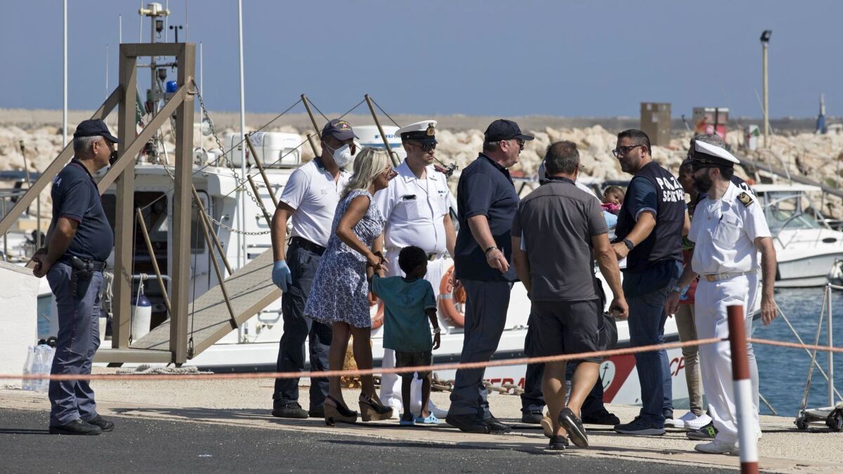 Migrant women and children are assisted by medical staff and law enforcement officers after disembarking from an Italian Coast Guard ship in the port of Pozzallo on Sunday.