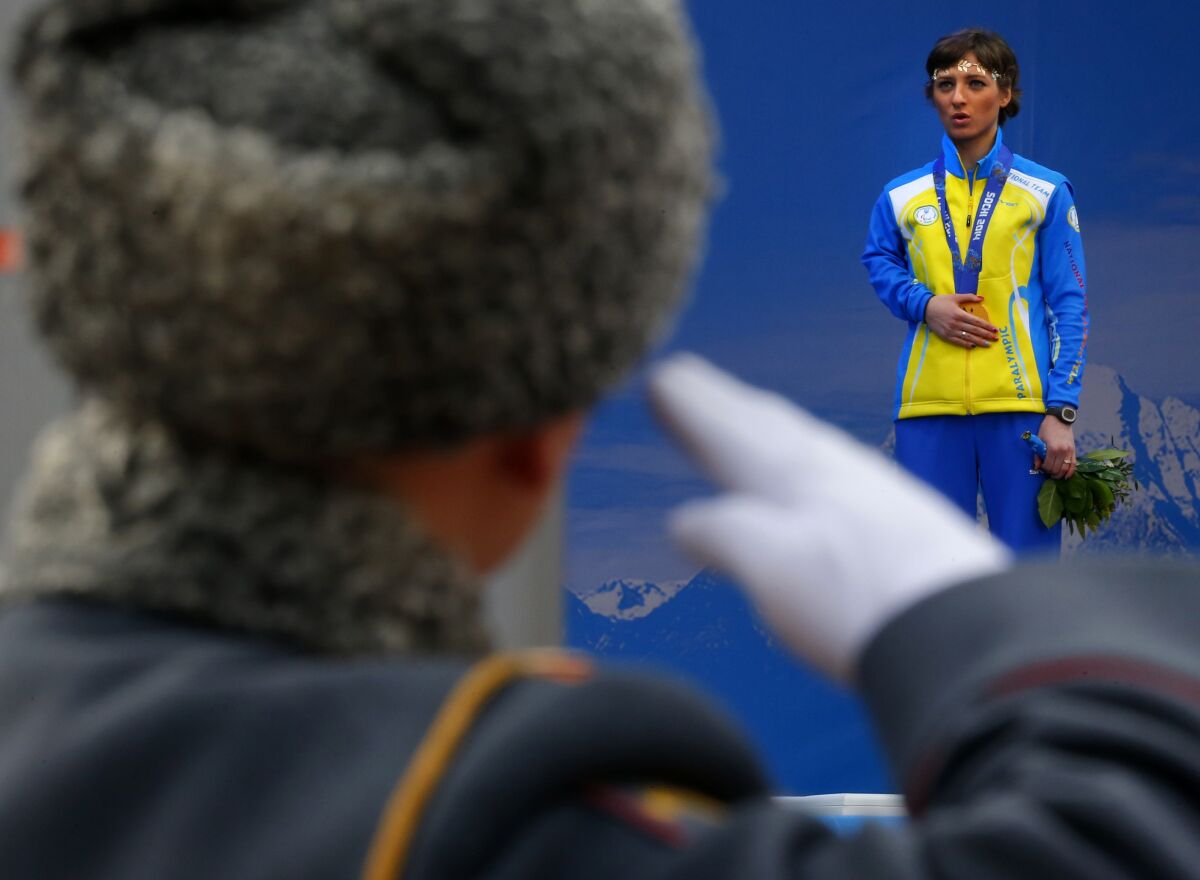 FILE - A Russian honor guard soldier salutes as Ukraine's Oleksandra Kononova covers her gold medal with her hand after winning the women's biathlon 12.5 km. standing event during a medal ceremony at the 2014 Winter Paralympic, Saturday, March 15, 2014, in Krasnaya Polyana, Russia. None of the 20 athletes from the Ukrainian Paralympic team have reached Beijing with the 2022 Paralympic Games opening at the end of the week, the International Paralympics Committee said Monday. (AP Photo/Dmitry Lovetsky, File)