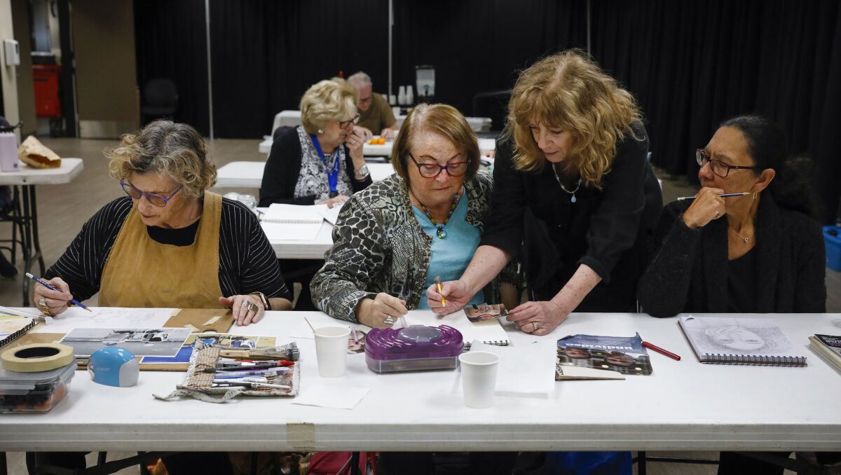 Two senior women work with an instructor at a basic drawing class at the community center.