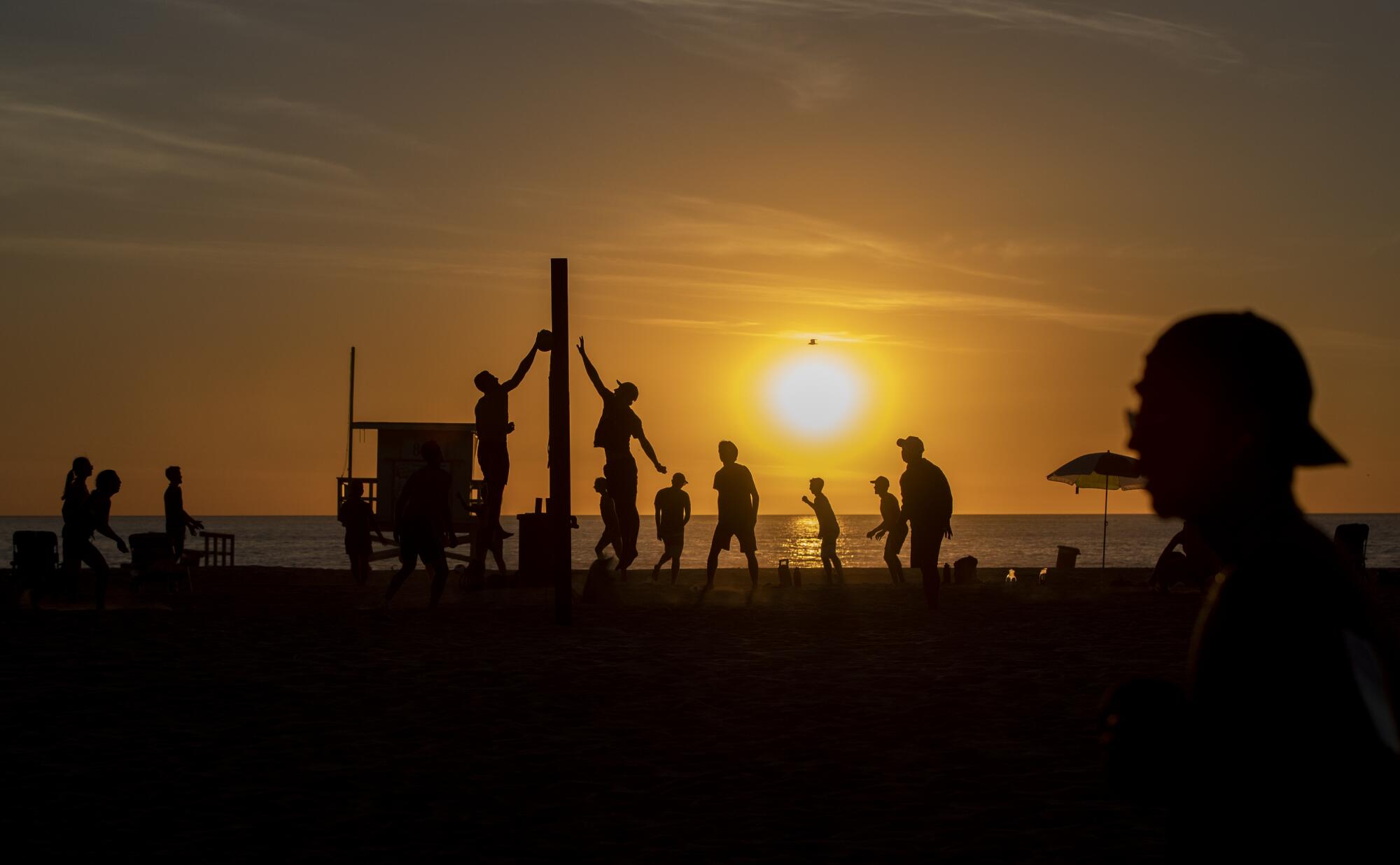 People are seen in silhouette playing volleyball at the beach as the sun sets.