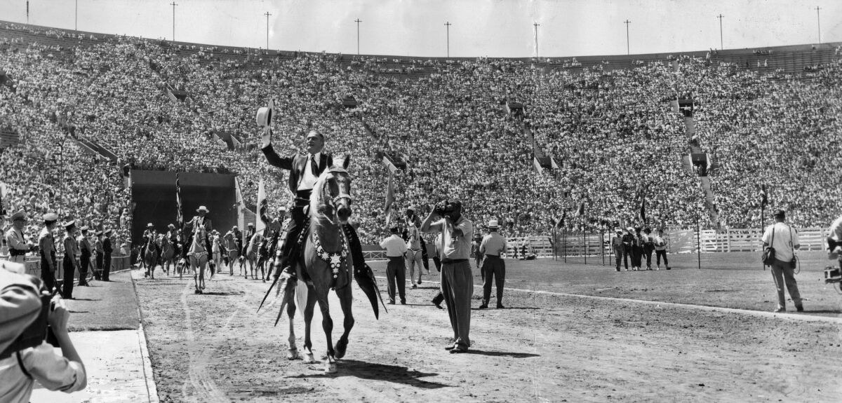 L.A. County Sheriff Eugene Biscailuz on horseback waving to a crowd at the Coliseum. 