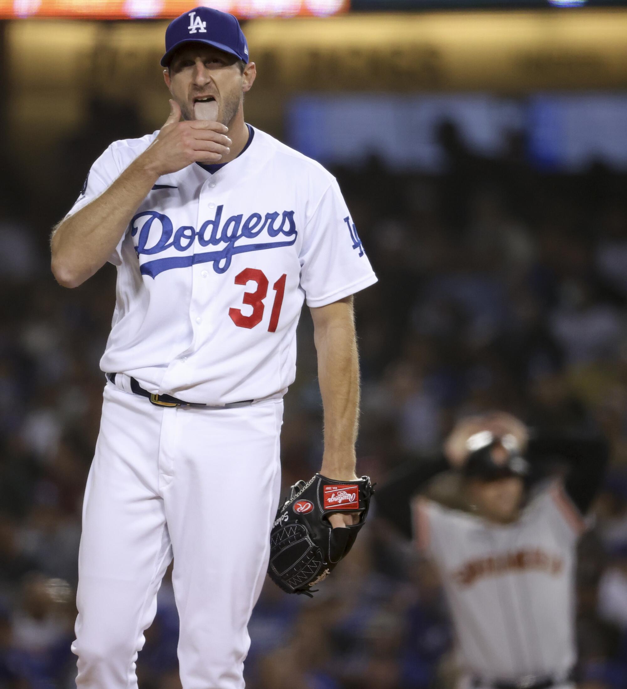 Los Angeles Dodgers starting pitcher Max Scherzer licks his fingers while preparing to pitch