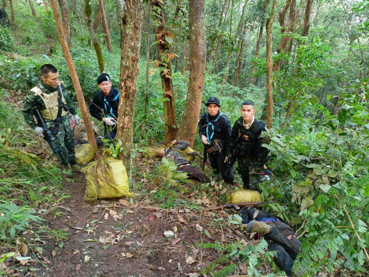Thailand soldiers stand with seized packages of illegal drugs and the body of a suspected smuggler at the scene of a gunfire exchange a day earlier in the Fang district in Chiang Mai, northern Thailand, Thursday, Dec. 8, 2022. Thai soldiers clashed with suspected drug smugglers in a forested area in the country's north near the Myanmar border, killing 15, authorities said Thursday. (Pha Muang Force via AP)