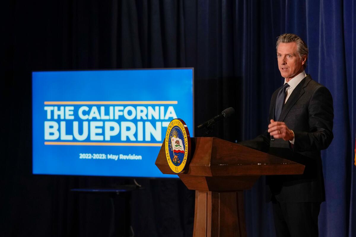 A man stands at a lectern next to a TV screen.