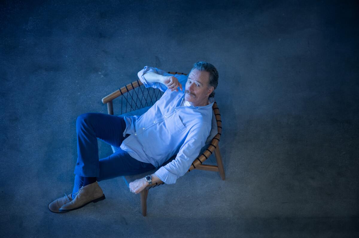 Bryan Cranston sits in a chair looking up for a portrait shot from above.