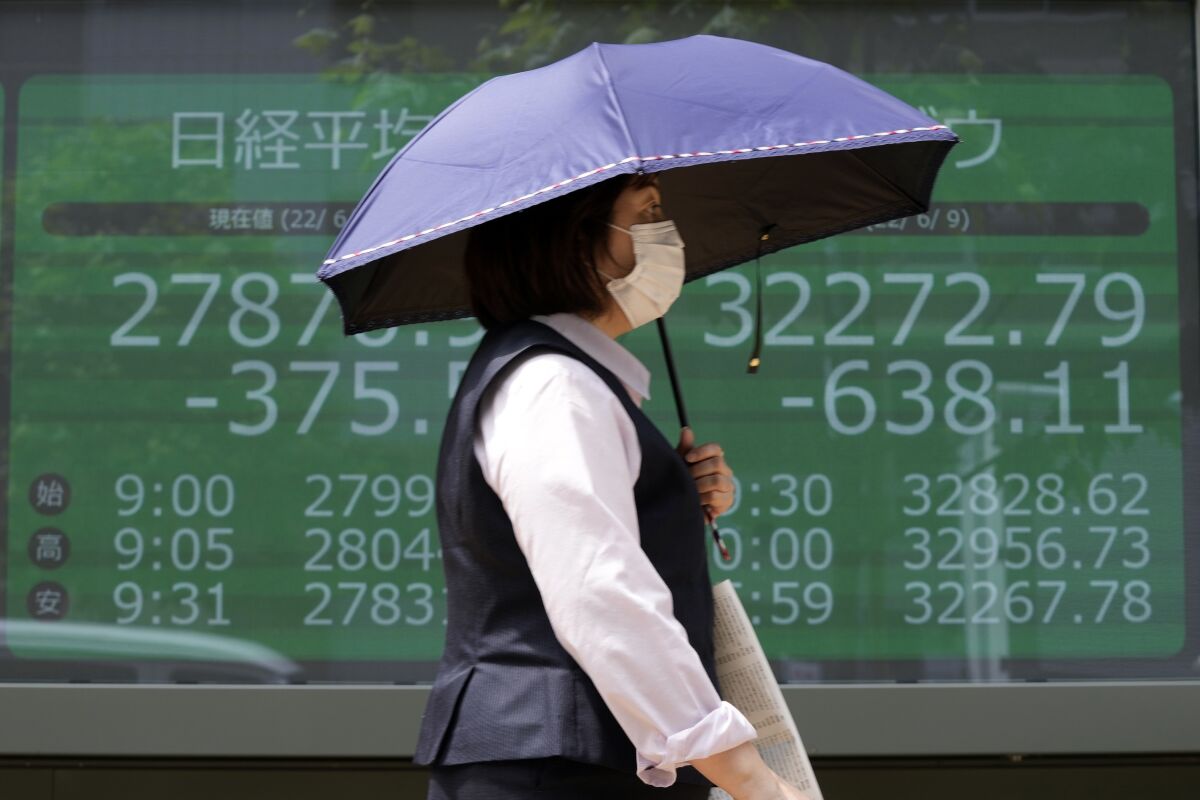 A woman wearing a protective mask in front of an electronic stock board showing Japan's Nikkei 225 and New York Dow indexes at a securities firm Friday, June 10, 2022, in Tokyo. Shares were mostly lower in Asia on Friday, with only Shanghai rising, after stocks tumbled on Wall Street on expectations central banks will focus on battling inflation with interest rate hikes. (AP Photo/Eugene Hoshiko)
