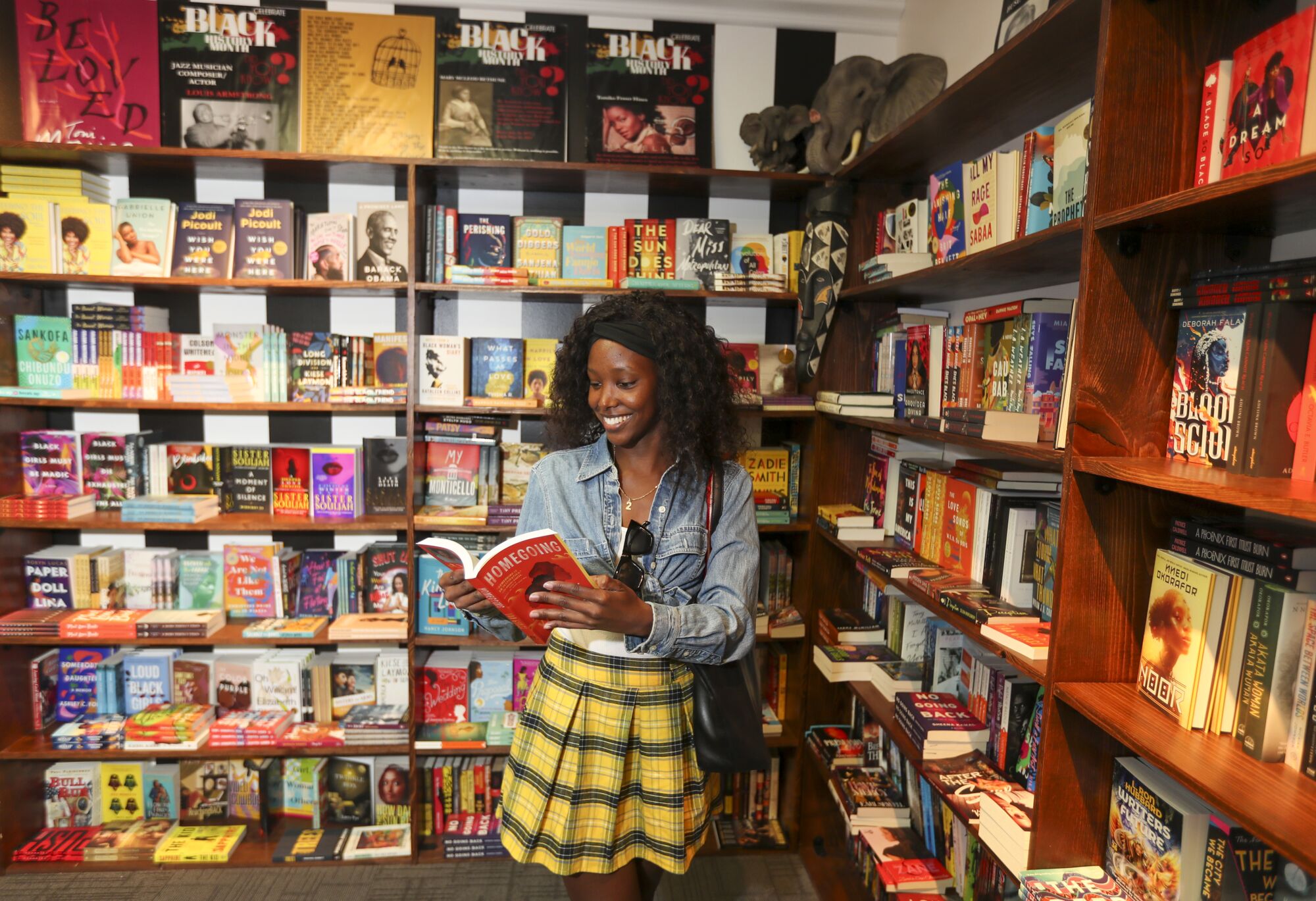 A woman with curly black hair reading a red book in front of a bookshelf.
