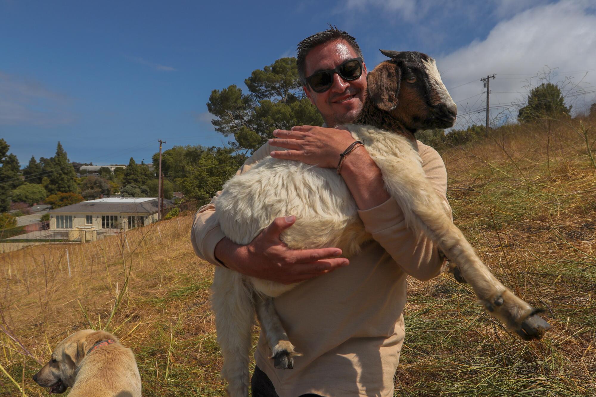 Cris Sarabia holds a goat on a hillside.