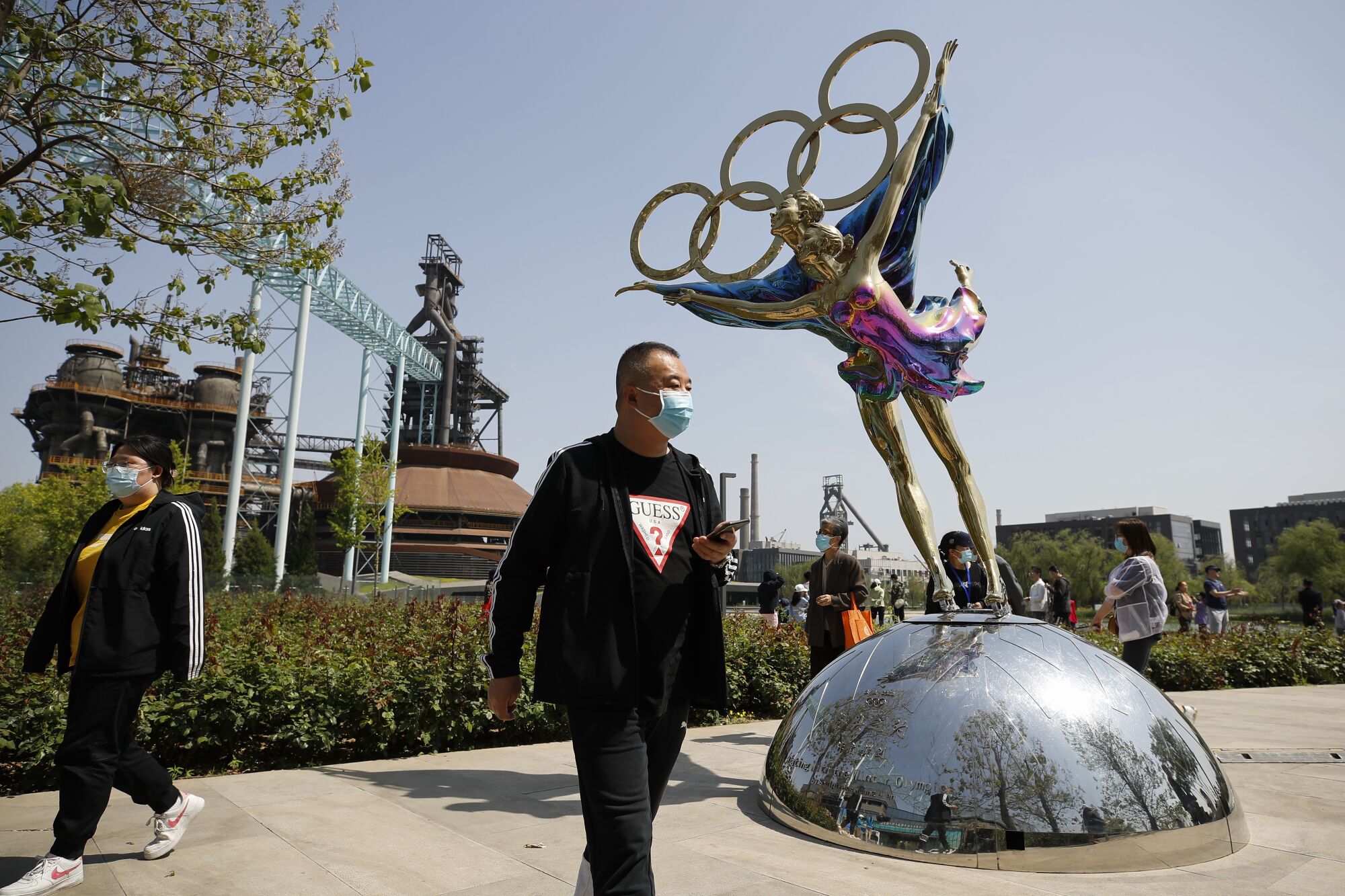 Visitors wearing face masks walk by a statue featuring Winter Olympics figure skating at the Shougang Park in Beijing