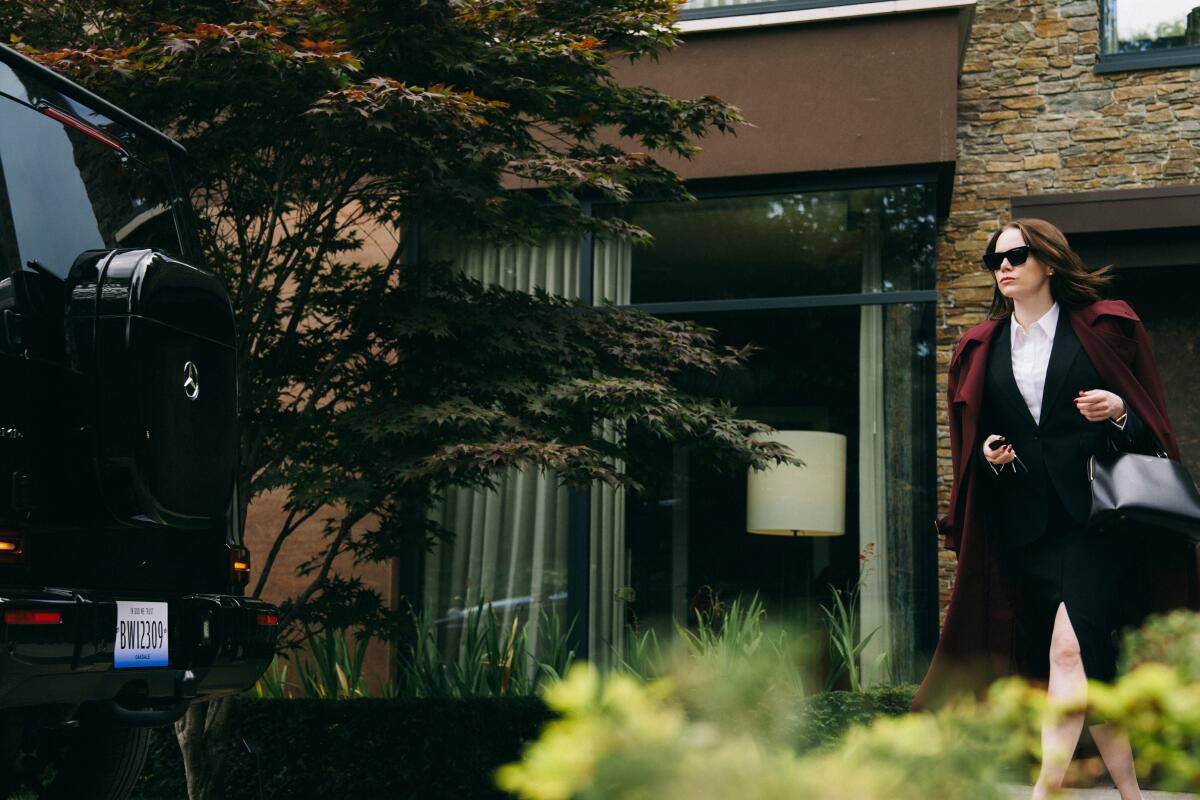 Emma Stone, in a black skirt suit and sunglasses, walks to her Mercedes SUV in "Bugonia."
