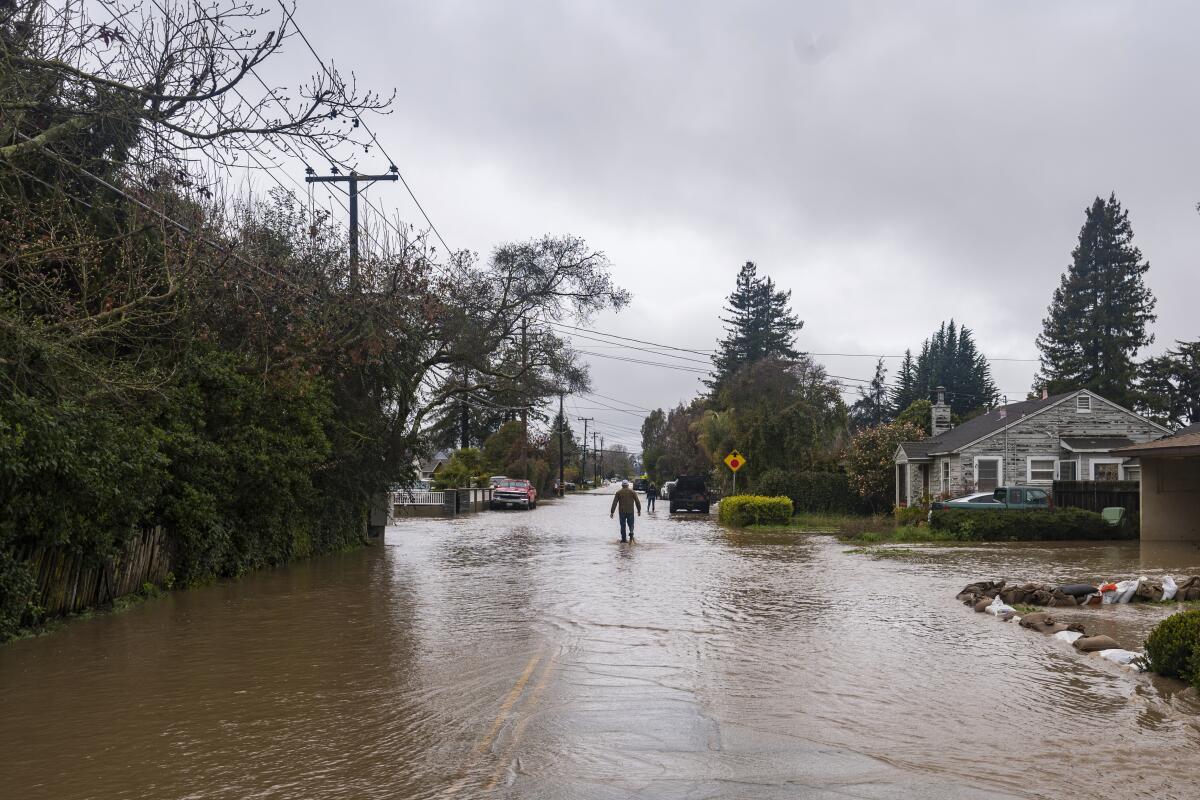 A man walks through floodwaters on a street next to houses