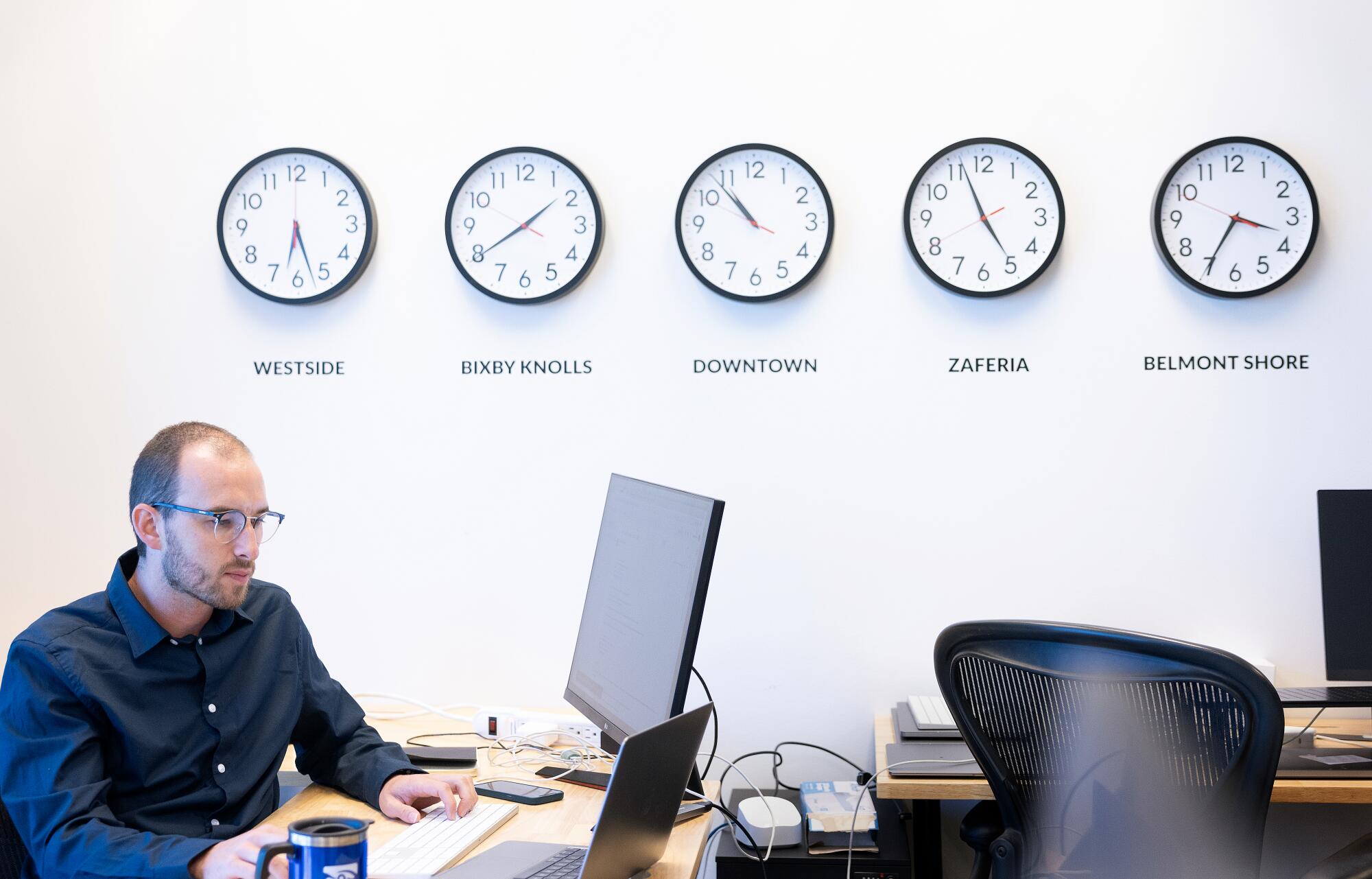 A man types on a keyboard along a wall lined by clocks