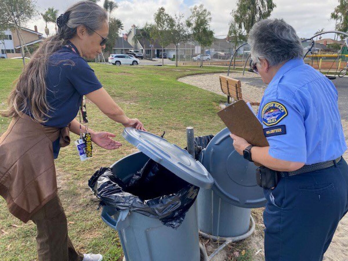 Volunteers with Huntington Beach's Wildlife Watch examine an unsecured garbage bin.
