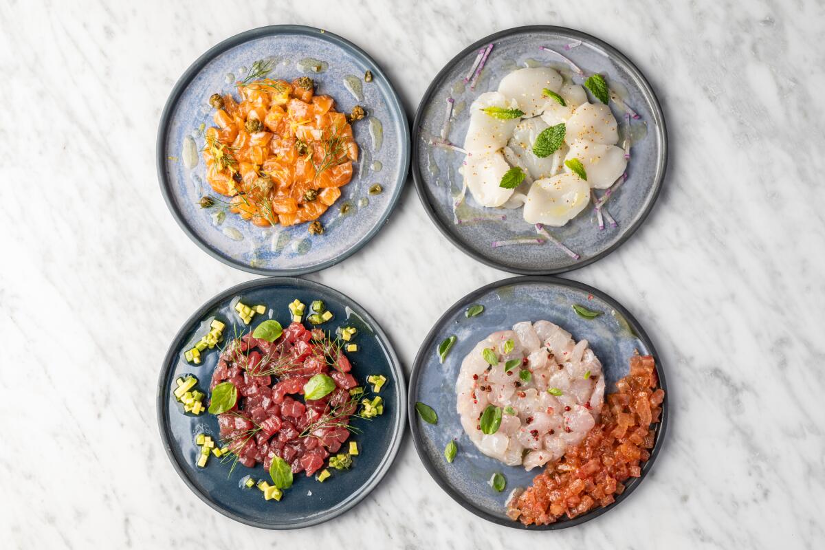 An overhead photo of four crudo dishes on round gray plates
