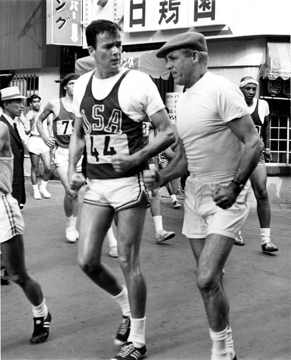 A black-and-white picture of a man, left, in a USA running uniform and a man in all-white gym clothes 