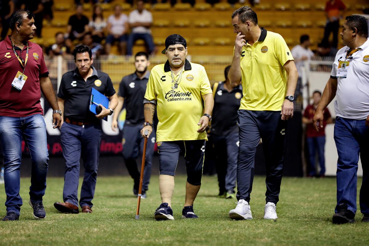 Diego Maradona uses a cane as he walks to the bench before the start of the game