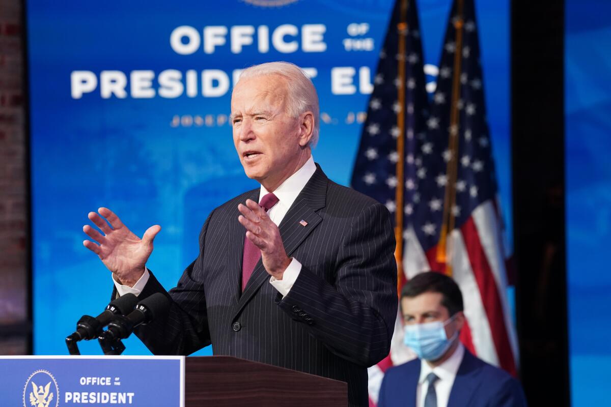 President-elect Joe Biden gestures as he speaks from a lectern on his transition office stage. 