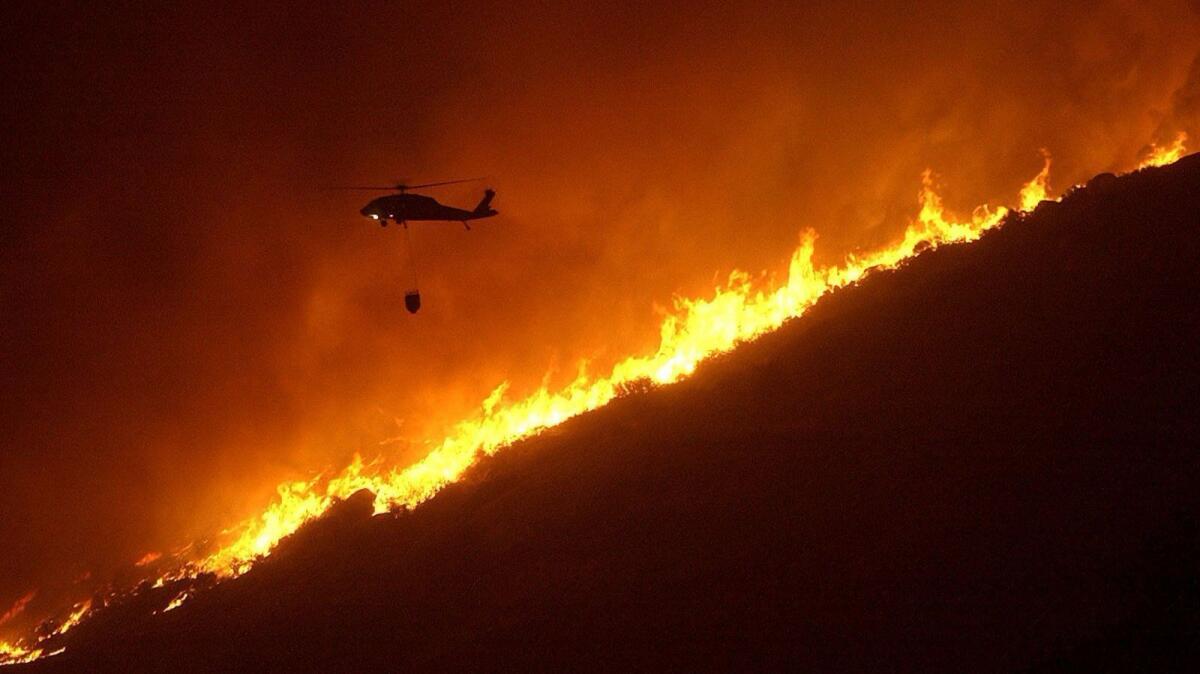 A water-dropping helicopter attacks flames in the town of Descanso, east of San Diego, while fighting the Cedar fire in 2003.