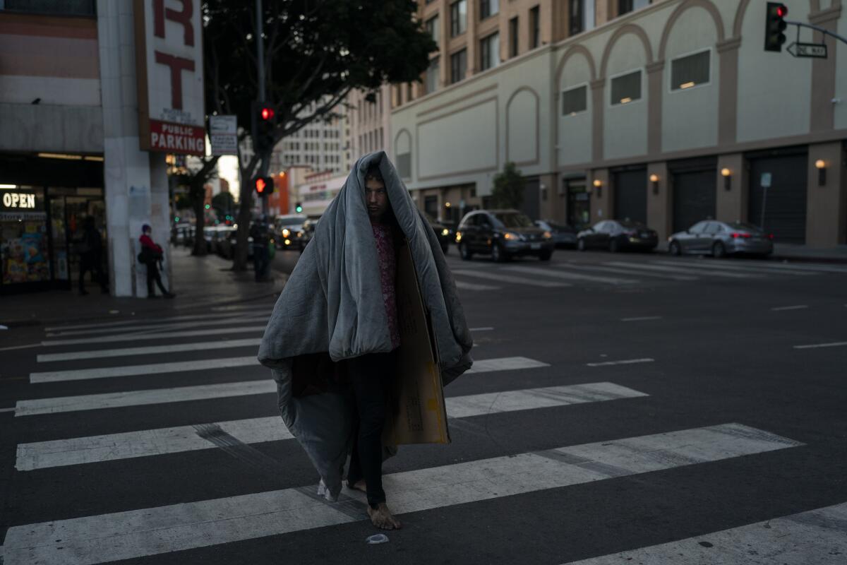 A homeless man walks across the street with a thick blanket over him in downtown Los Angeles on April 15. 