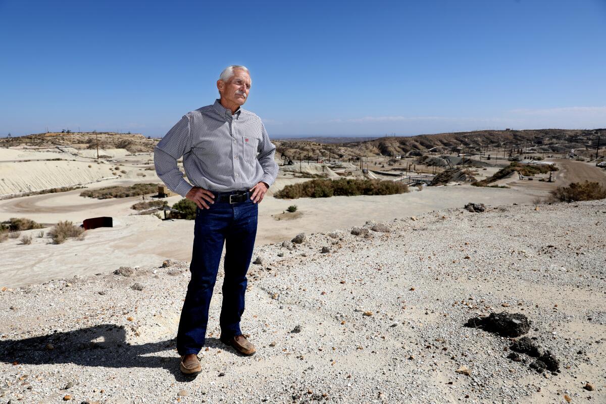 A man on barren land with oil equipment in the background