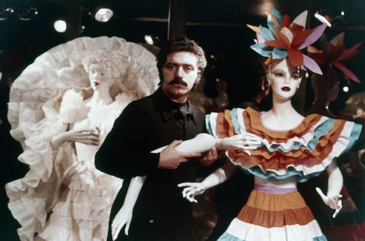 A man with a mustache is flanked by two mannequins wearing paper dresses