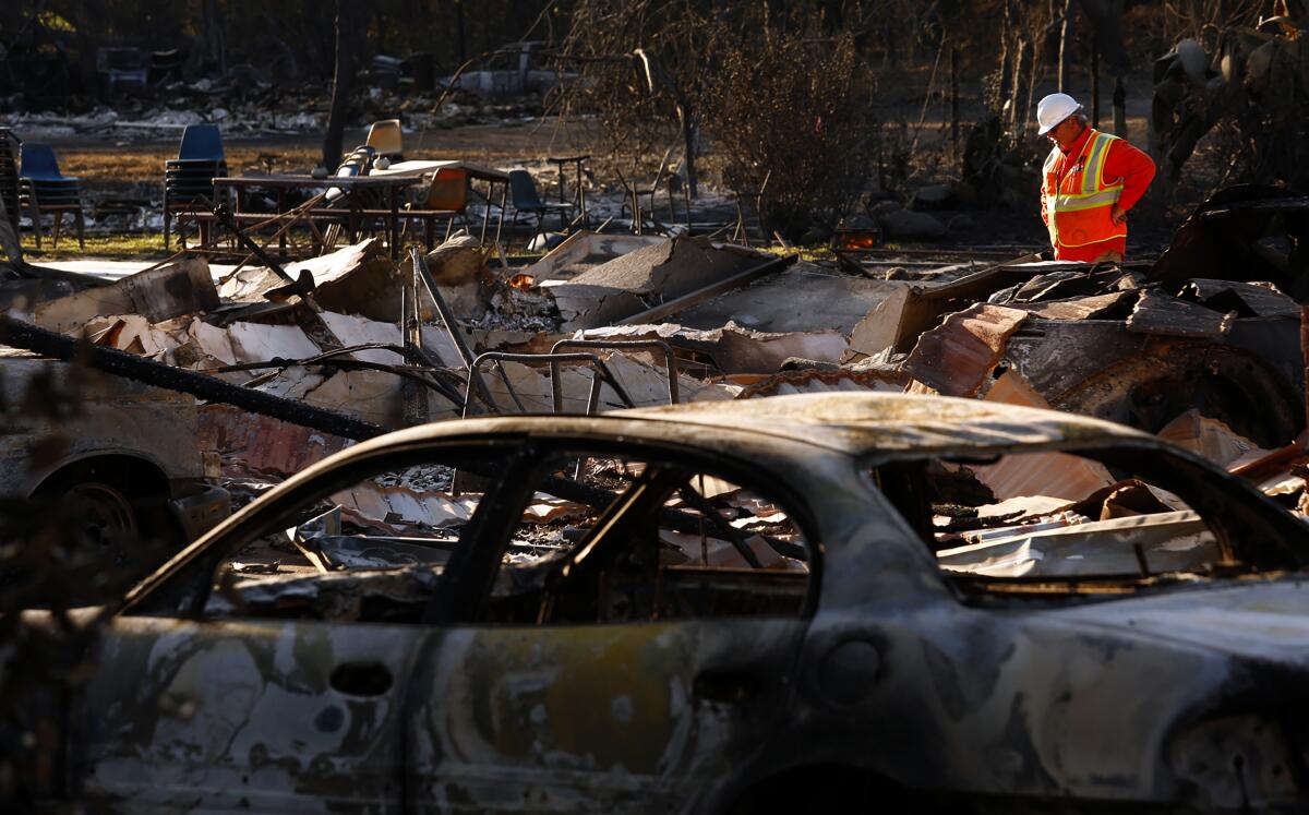 A worker in a reflective vest and hardhat eyes the remains of burned vehicles. 