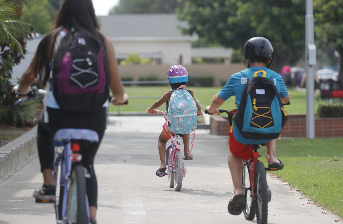 A family of siblings ride away with new school backpacks during a distribution of back-to-school supplies on Friday.