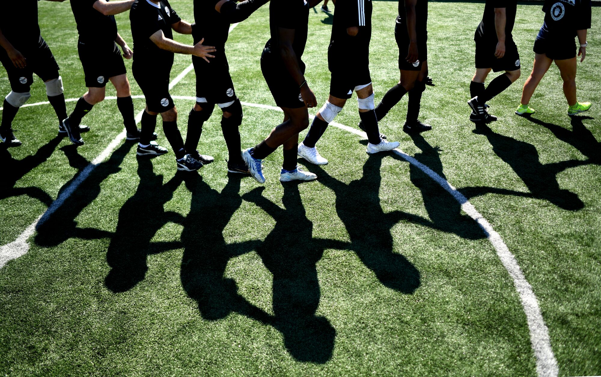 Blind soccer players hold on to one another for balance and direction as they walk in a line off a field during a water break