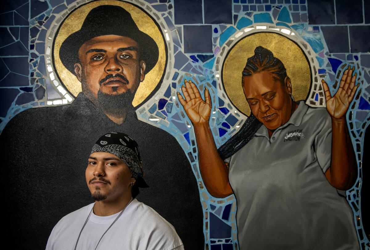 A young man with a black bandanna on his head in front of a mosaic-style mural with realistic images of 2 people with halos