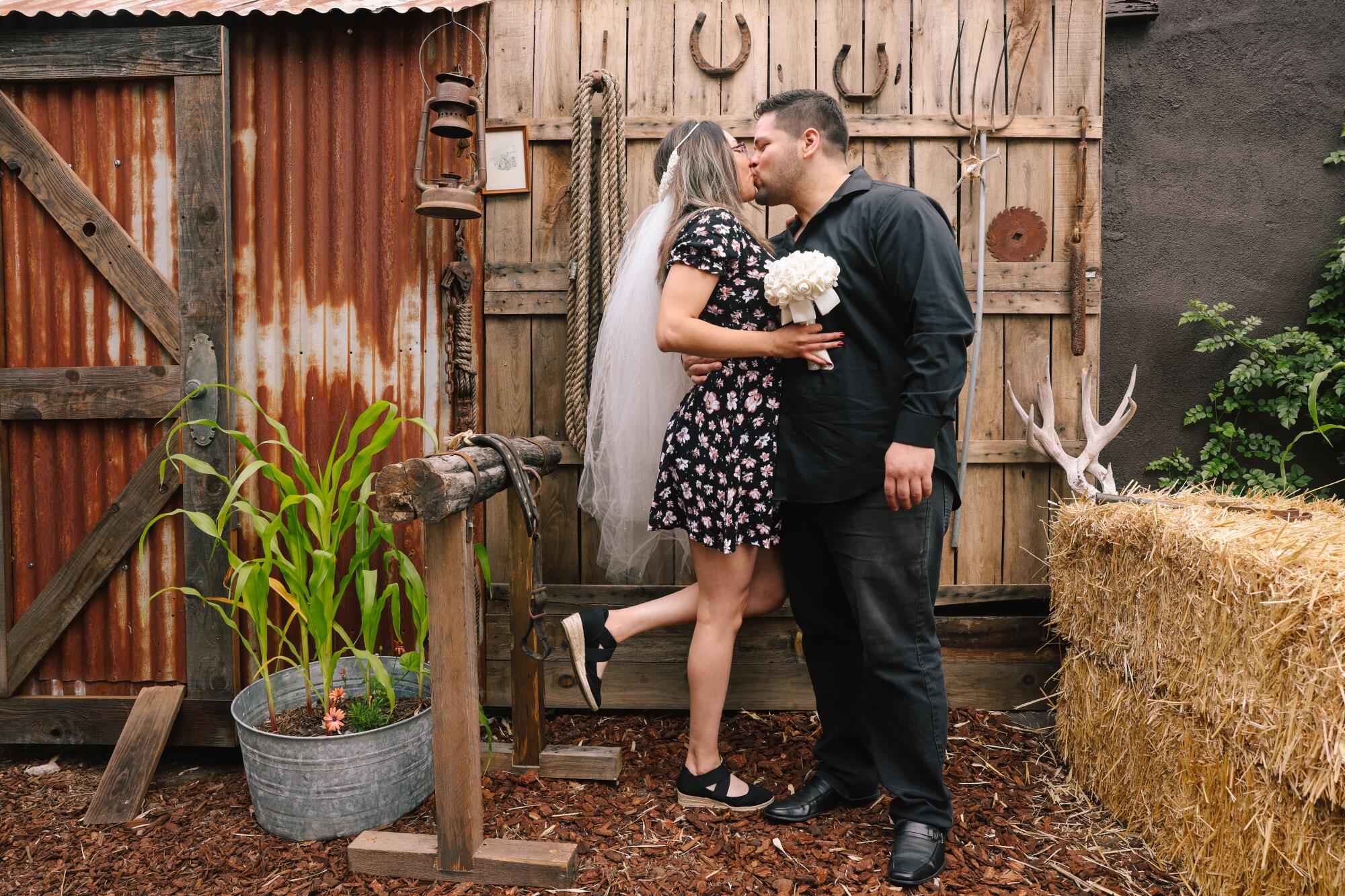 A woman and a man kiss in front of a farmhouse-themed wall