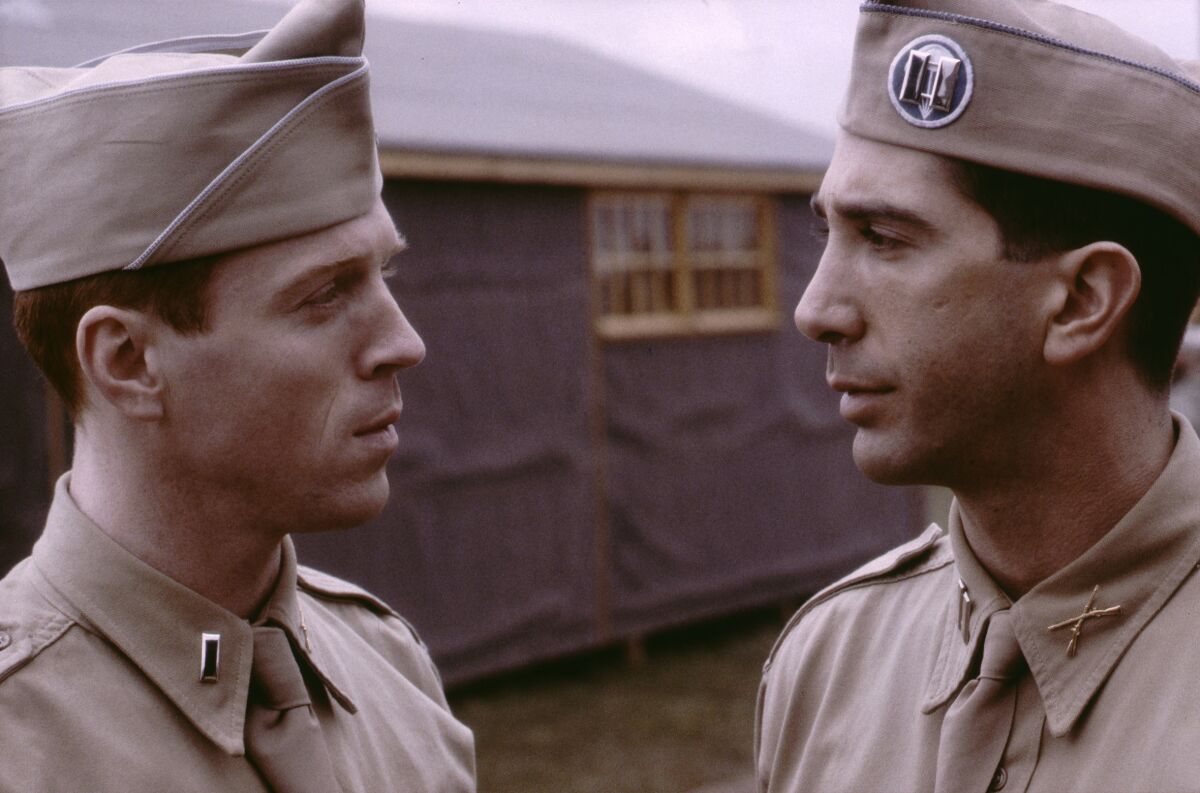 Two men in military uniform stand beside a building.