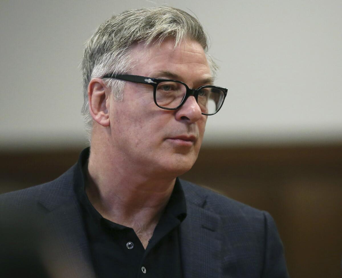 Alec Baldwin wearing dark-rimmed glasses and a blazer