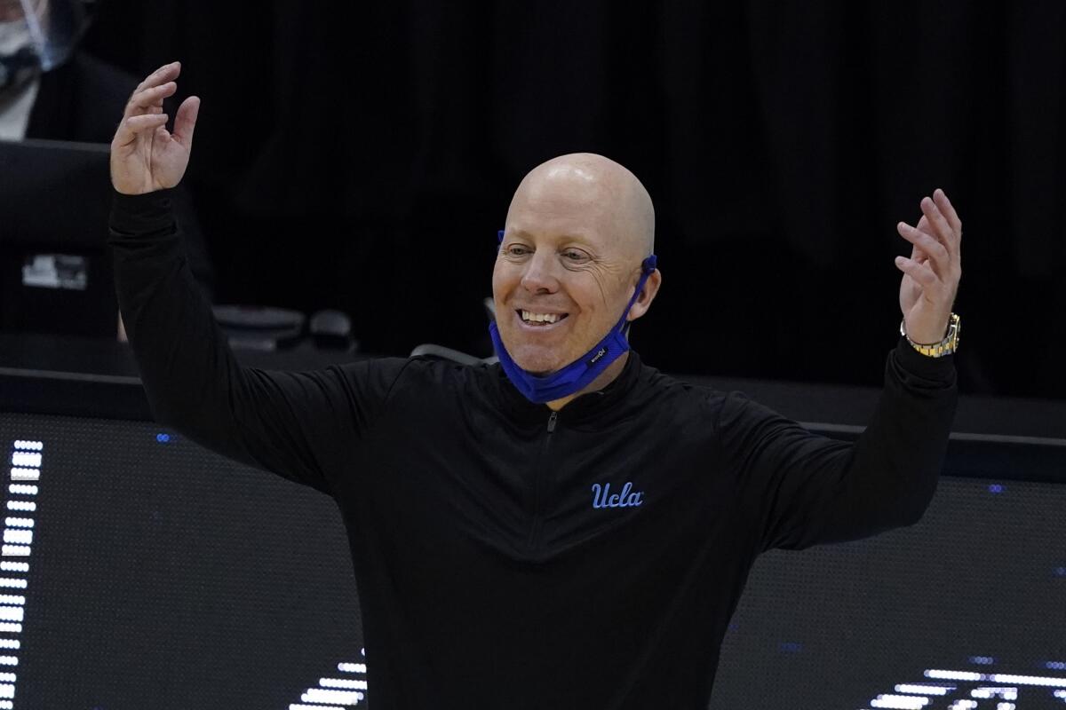 UCLA coach Mick Cronin raises both arms and smiles.