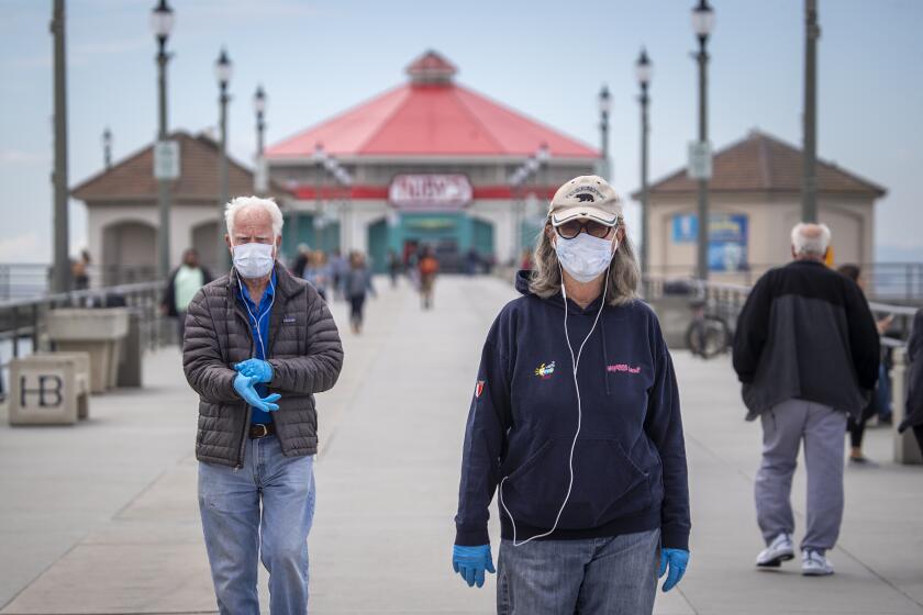 HUNTINGTON BEACH, CALIF. -- WEDNESDAY, MARCH 18, 2020: Dr. Dallas Weaver, 79, and his wife, Janet Weaver, 75, of Huntington Beach, wear their reusable protective masks and gloves that they will place in the oven and heat up to 160-degrees (clothes will be put in the dryer) after their return from walking on the Huntington Beach pier amid coronavirus pandemic restrictions in Huntington Beach, Calif., on March 18, 2020. "We are wearing masks to protect other people and keep ourselves from touching our faces," said Dr. Dallas Weaver. Orange County bars, breweries and wineries were ordered to close, restaurants were told to offer take-out or delivery only, and people were told not to gather to curb transmission of the coronavirus. (Allen J. Schaben / Los Angeles Times)