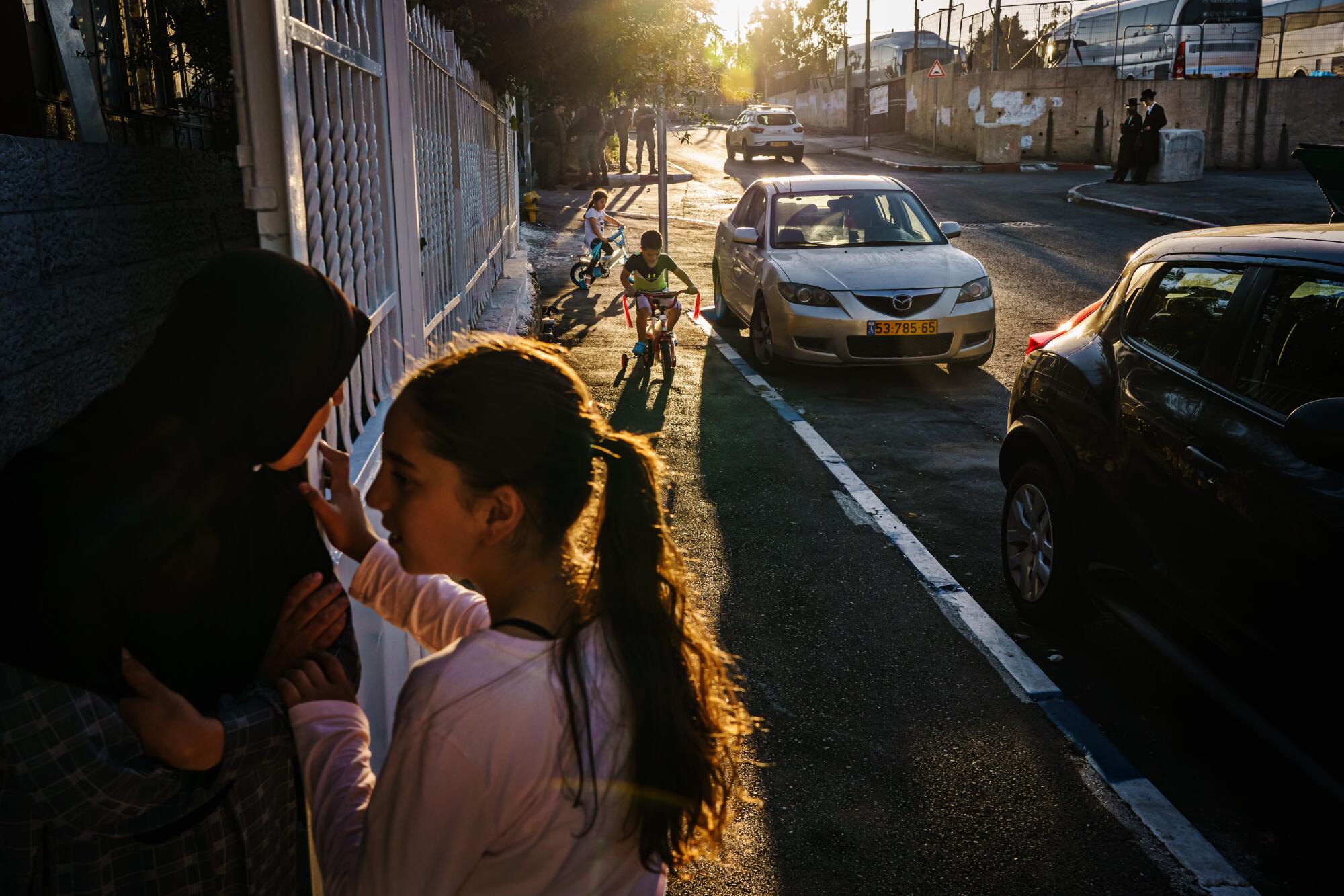 The evening sun casts long shadows a street as children play.